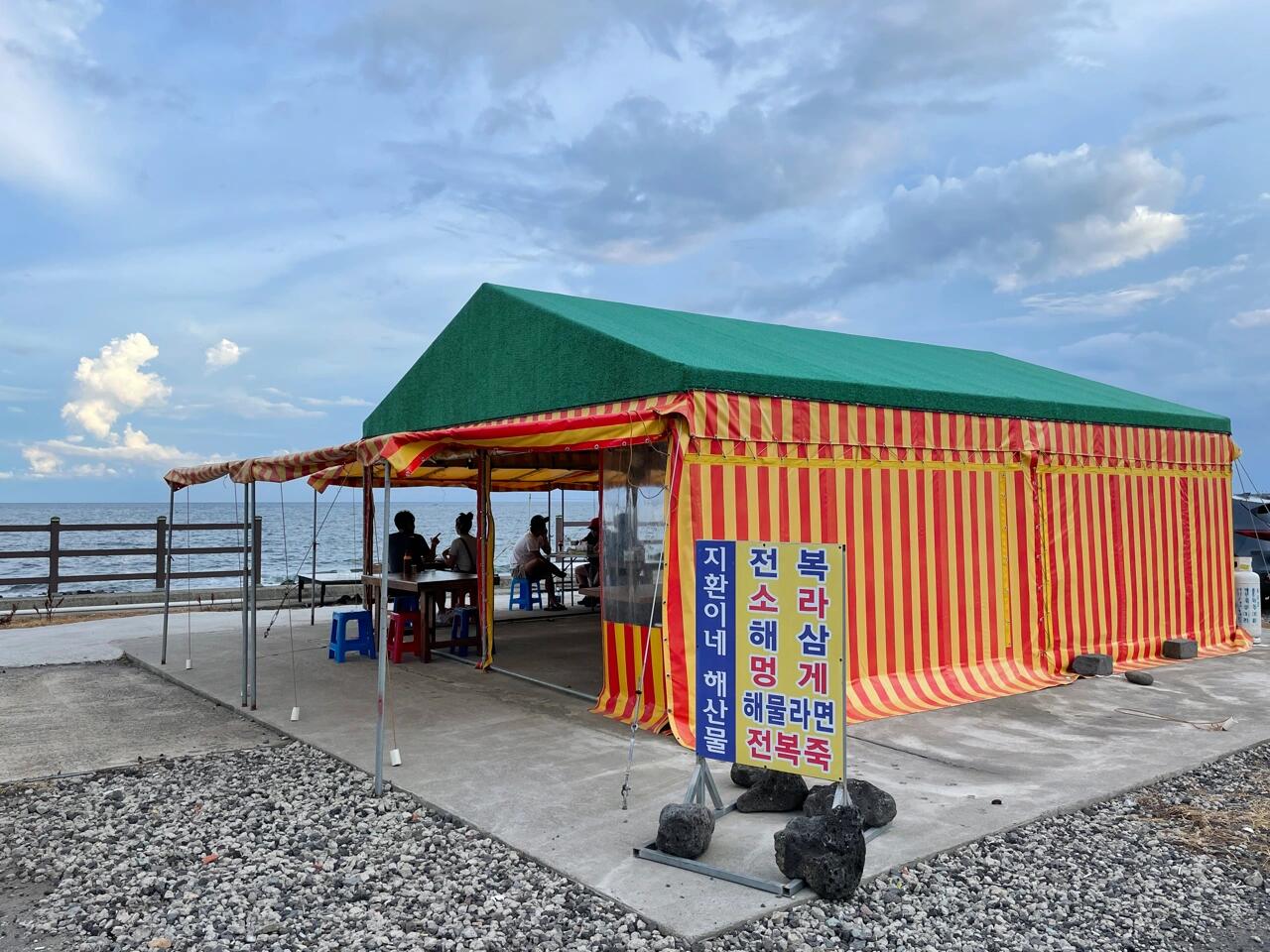 
                        韓國濟州島海邊的海鮮拉面??在濟州島的城山日出峰附近，城山邑的海邊有一家超吸引人的大排檔??。濟州島的大排檔不多，尤其是海邊的，所以特別受歡迎。有次和首爾來的朋友們一起去嘗試了這里的海鮮拉面和小魷魚生魚片，真的超級美味??！雖然這里的海鮮拉面里沒有螃蟹和章魚，但是有超多蝦和紅蛤等海鮮，湯頭也是超級贊的，是那種辣而不油的干爽辣湯頭，配上一杯米酒??，簡直是美食的最佳搭檔！ps：不太確定冬天是否營業，但如果夏天傍晚來這里，絕對是享受美食的最佳時光～??